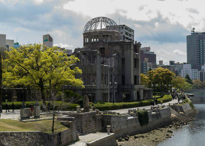 The iconic Hiroshima Genbaku Dome, framed by lush green trees and a gentle river.